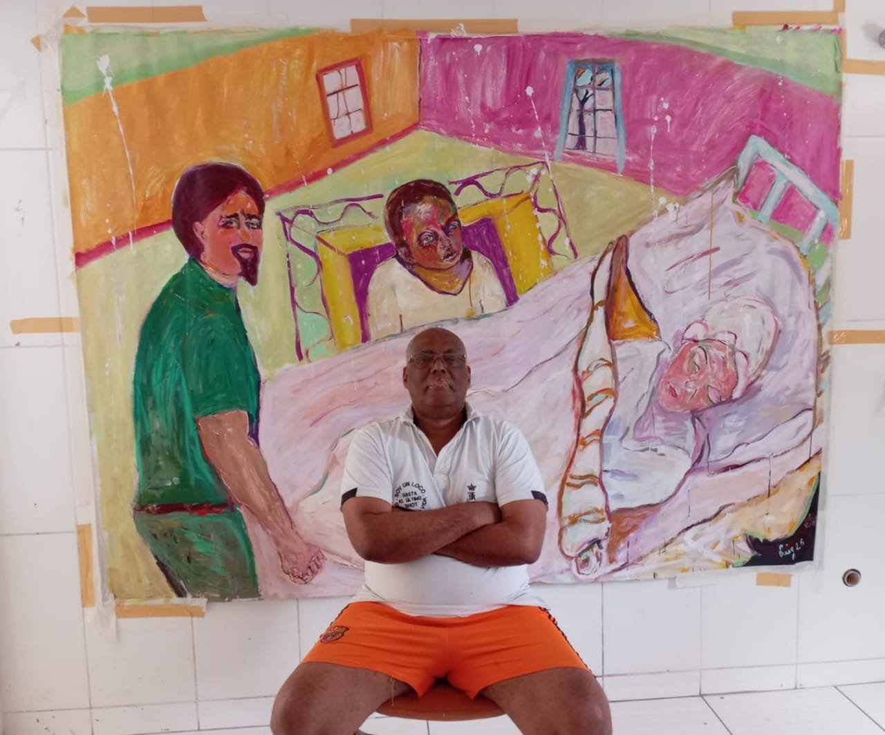 Víctor Alexis Puig sentado ante una obra cromática rosa-cadmio con tres figuras